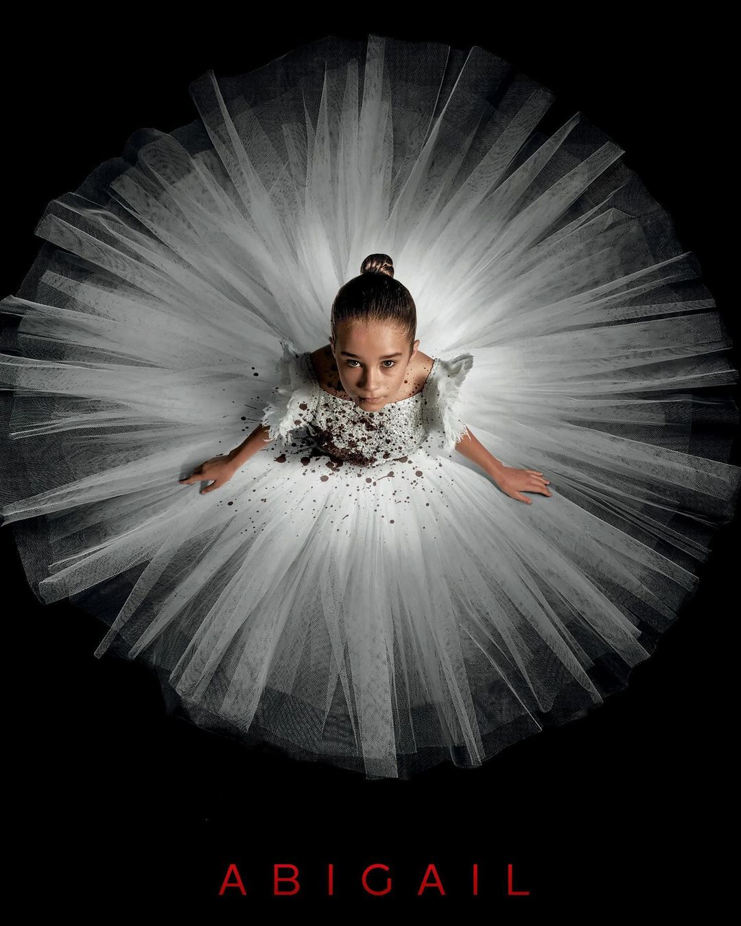 Eye-level shot of a young girl in a white tutu with brown accents against a black backdrop, looking up at the camera with a serious expression.