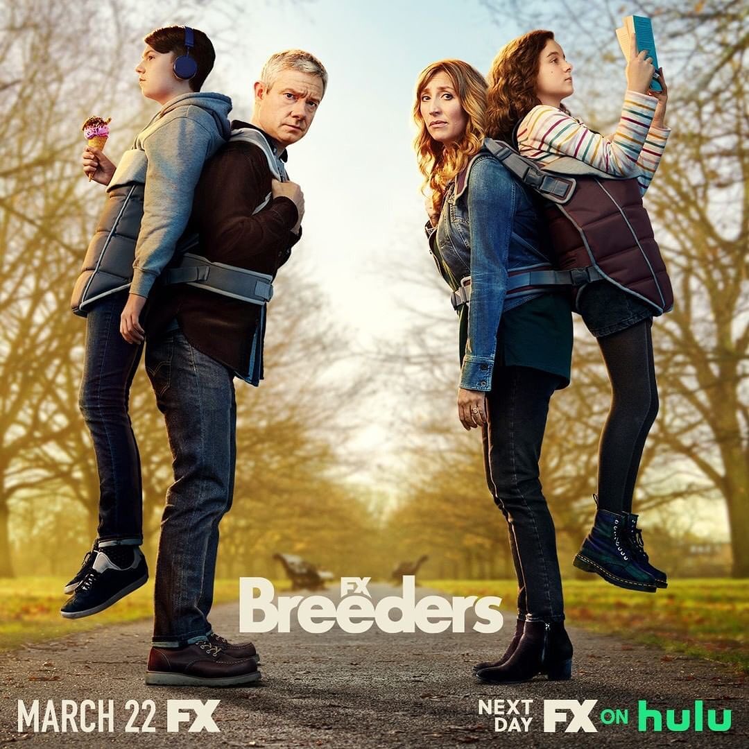 Promotional image for the TV series Breeders featuring two adults carrying two children in baby carriers in an outdoor environment.