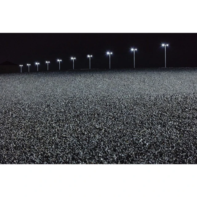 Wide outdoor shot at night features row of lights illuminating dark asphalt road, creating a stark contrast in a dark, desolate environment.