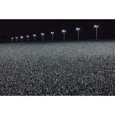Wide outdoor shot at night features row of lights illuminating dark asphalt road, creating a stark contrast in a dark, desolate environment.