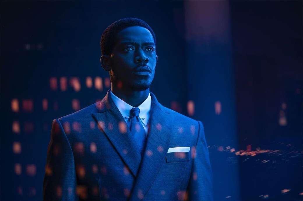 Dramatic portrait of an African American man in a suit against a blurred cityscape background with blue lighting and modern aesthetic.