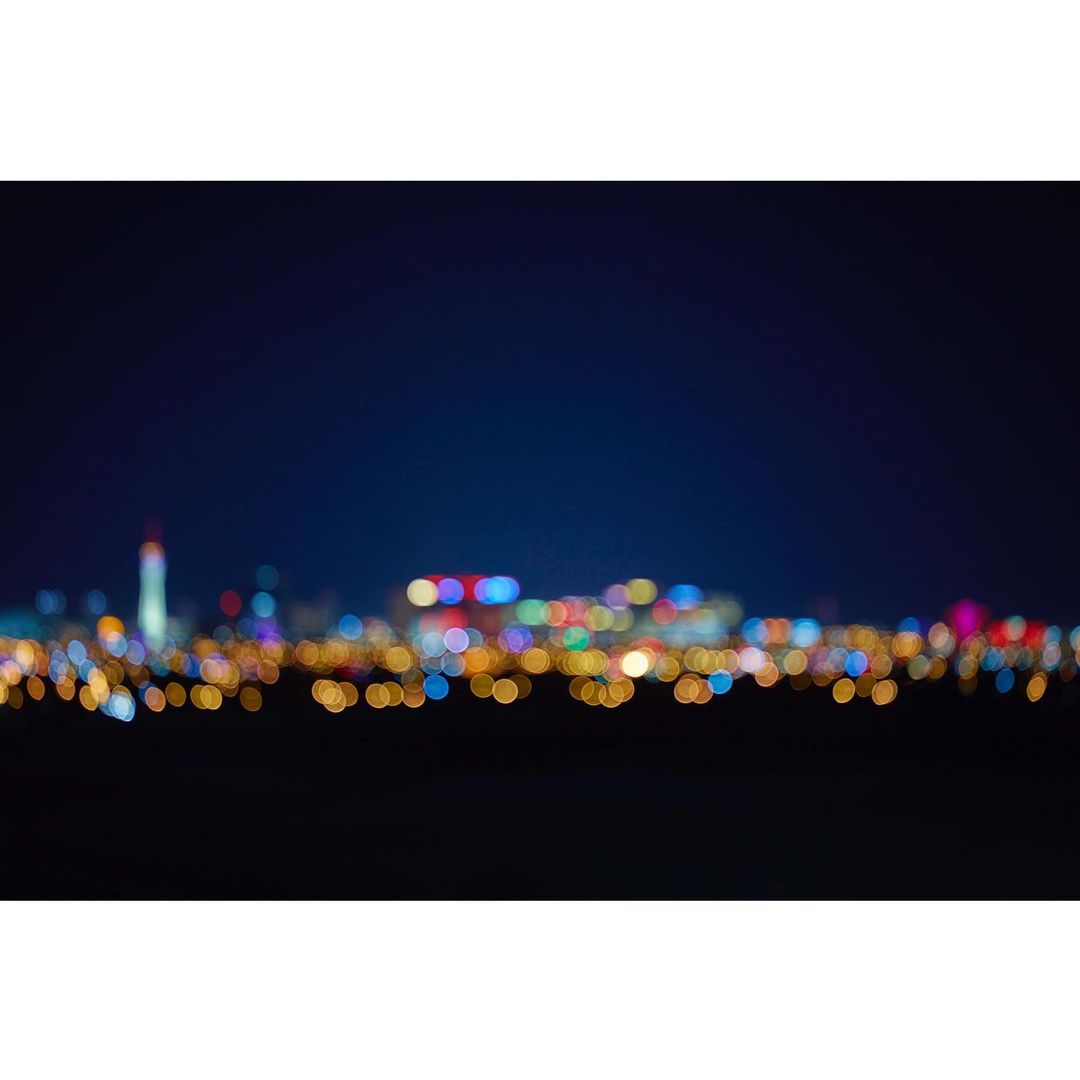 Blurred cityscape lights twinkle at night, creating a bokeh effect with orange, blue, and red hues against a dark sky.