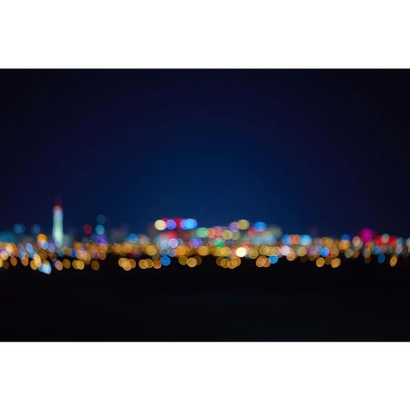 Blurred cityscape lights twinkle at night, creating a bokeh effect with orange, blue, and red hues against a dark sky.