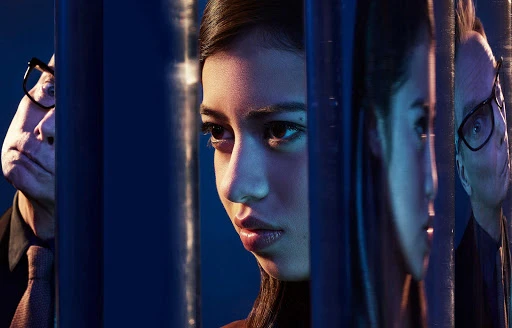 Portrait of a young woman and an older man behind vertical bars, split into sections, in a photo studio with blue backlighting.