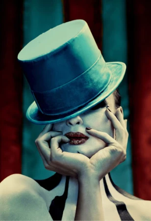 Close-up portrait of a woman wearing a teal top hat tilted over her eyes and dark lipstick by photographer Matthias Clamer