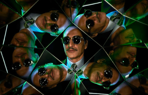 Kaleidoscopic mirrored reflection of a bald man wearing dark sunglasses, patterned tie, and suit photographed by Matthias Clamer.