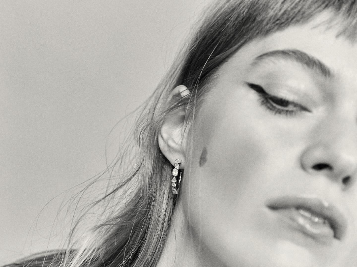 Close up monochrome portrait of a woman wearing diamond hoop earrings and winged eyeliner by Melanie and Ramon.
