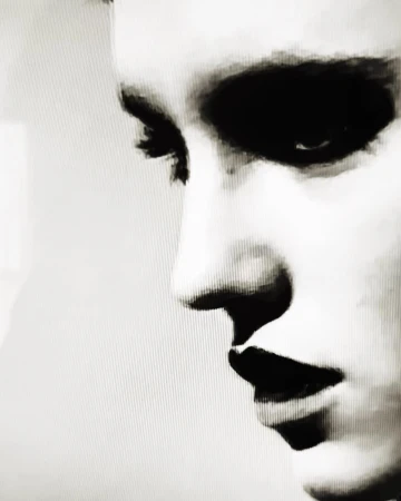 Close-up monochrome portrait of a person profile featuring high-contrast dark eye makeup and heavy grain texture.