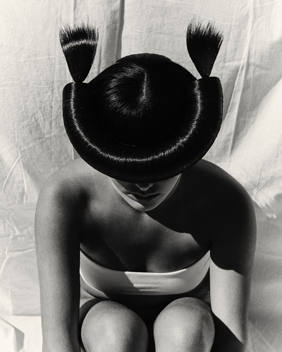Monochrome portrait of a woman with avant-garde sculpted black hair styling wearing a white bandeau top.