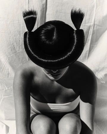 Monochrome portrait of a woman with avant-garde sculpted black hair styling wearing a white bandeau top.