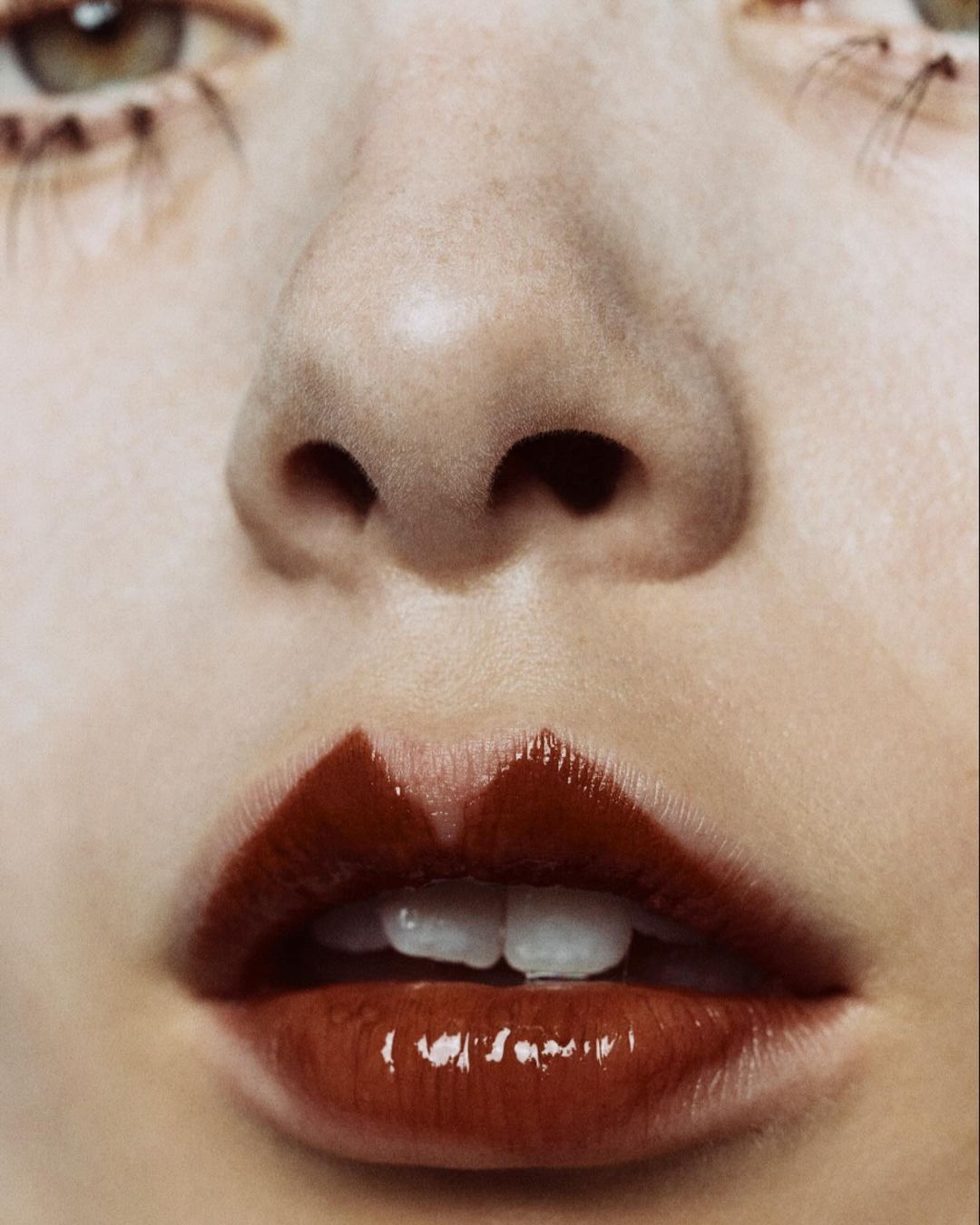 Close-up portrait of a woman's face with glossy dark red lips painted in a heart shape, pale skin, and light green eyes.