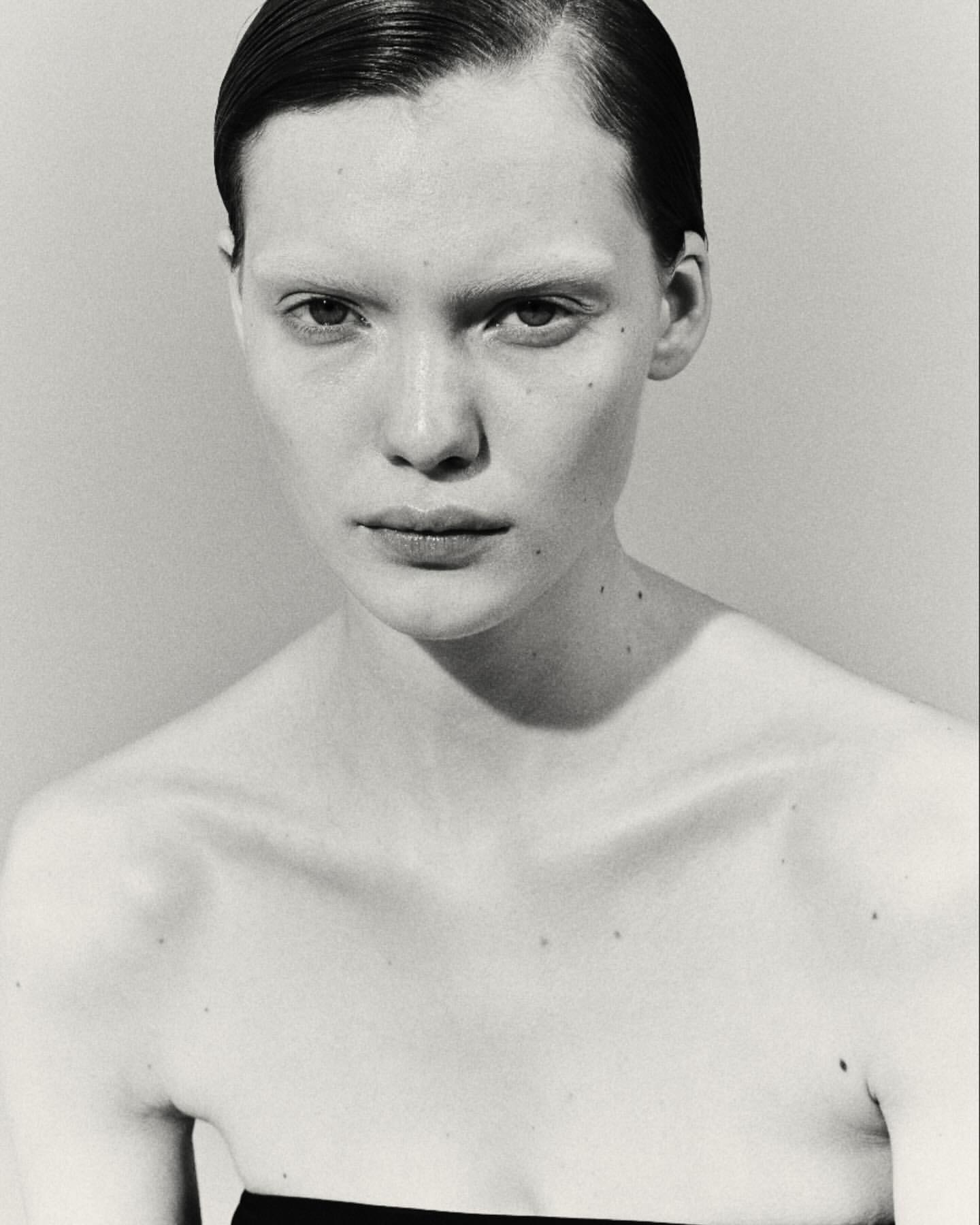 Striking black and white close-up of a fair-skinned young woman with sleek hair, gazing intently in a studio setting with neutral background.