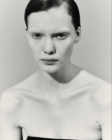 Striking black and white close-up of a fair-skinned young woman with sleek hair, gazing intently in a studio setting with neutral background.