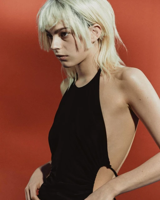 Adult woman poses in a black halter dress against a red background in a studio fashion-style portrait with side lighting.