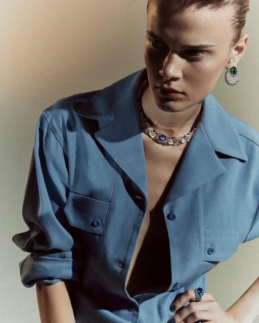 Fashion shot of a woman wearing a blue shirt and jewelry, including a necklace, ring, and earrings, in a studio setting.