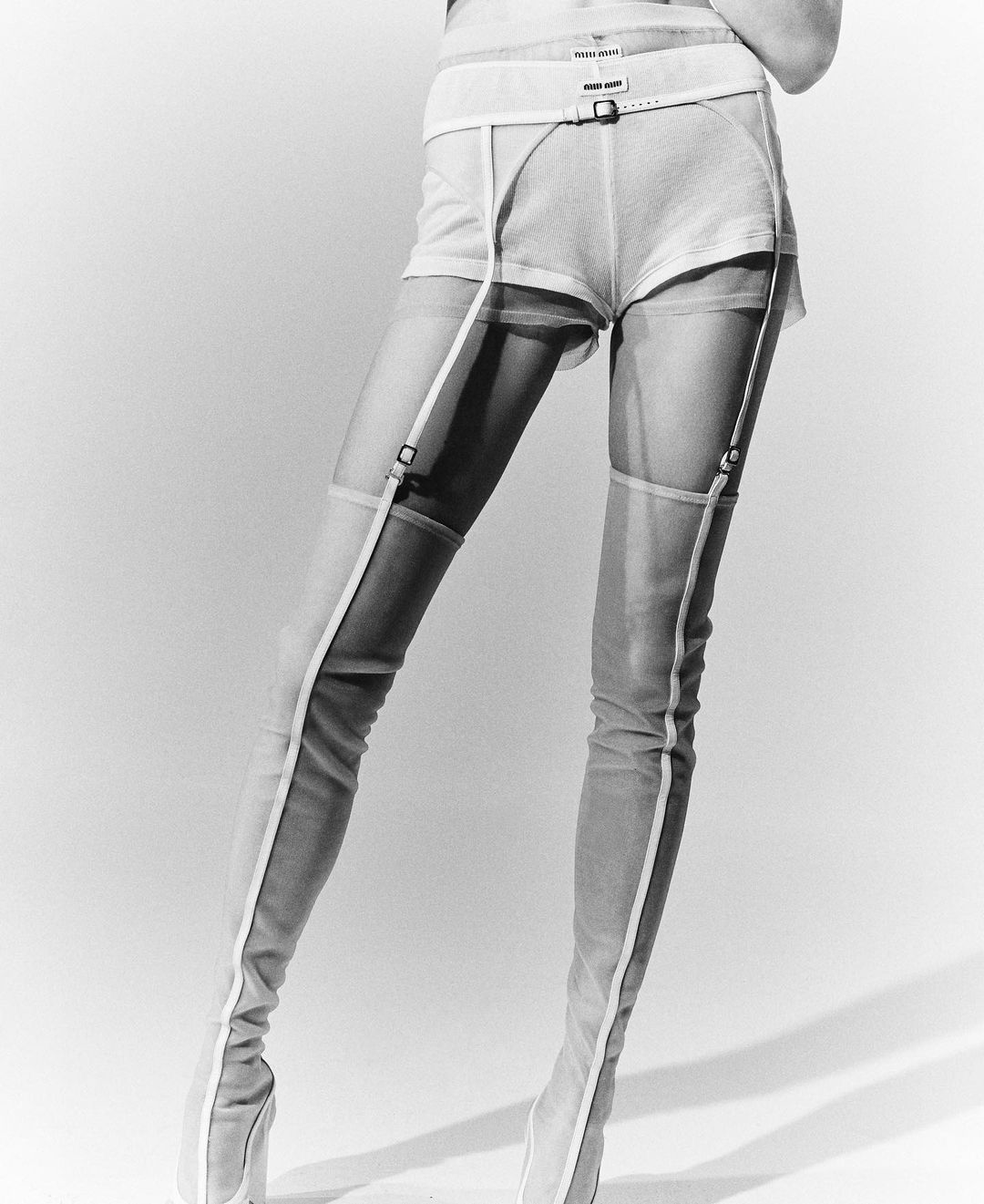 Fashionable women's thigh-high boots paired with shorts in a studio setting, showcasing a modern and edgy aesthetic. White backdrop.