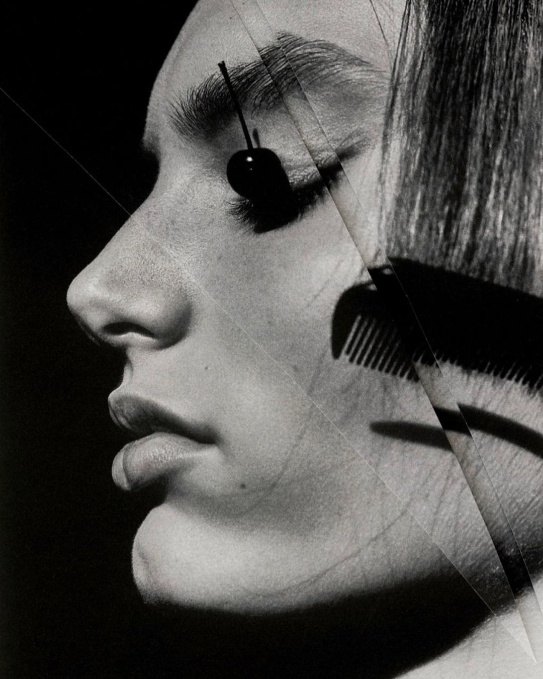 Monochrome portrait of a woman with a cherry over her eye and a comb overlaying her face, creating a striking and unusual visual.