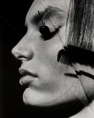 Monochrome portrait of a woman with a cherry over her eye and a comb overlaying her face, creating a striking and unusual visual.