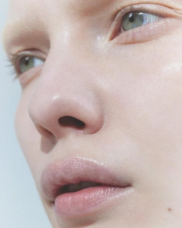 Close-up portrait of a person's face focusing on green eyes and glossy lips with natural skin texture against a white background.