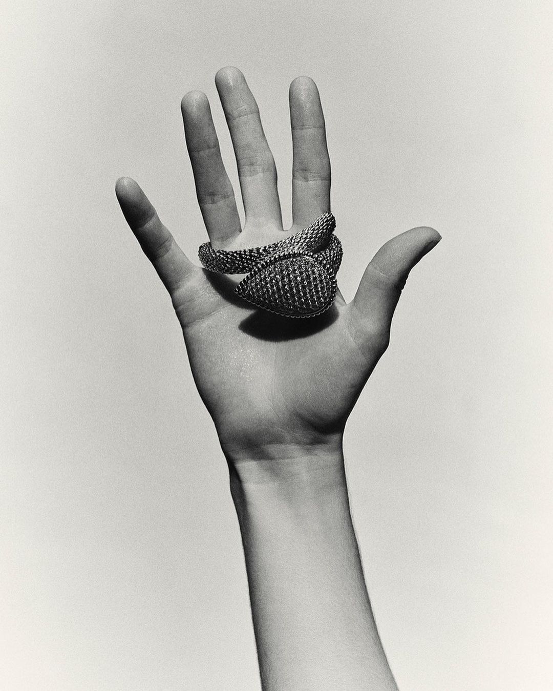 Close-up black and white studio shot of an adult hand with a woven metal cuff or accessory coiled around the fingers and hand.