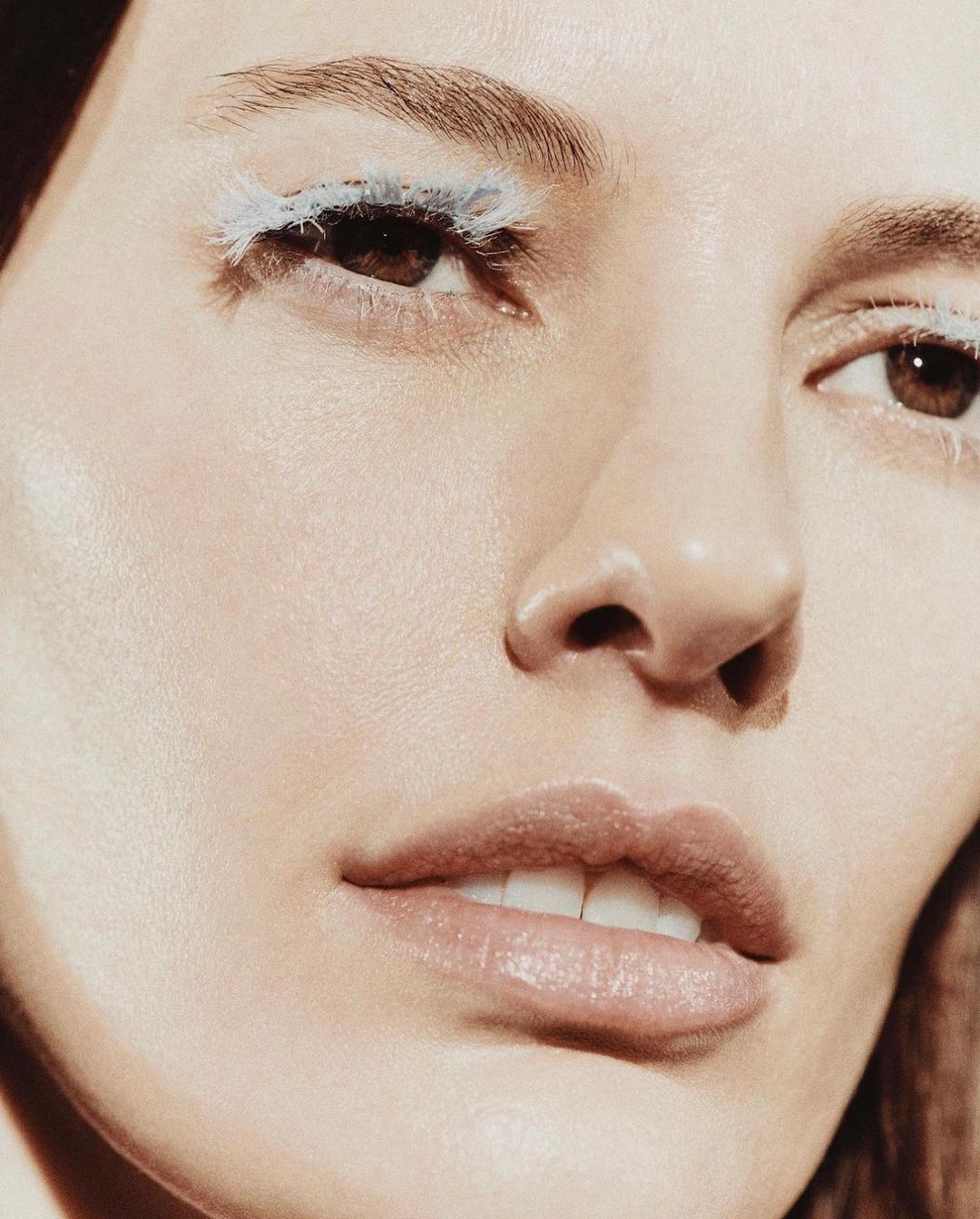 Close-up studio shot of a woman's face with light skin, light eyebrows, and brown eyes. She has dramatic white and light blue eyelashes.