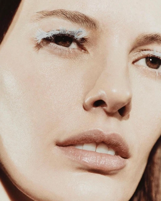 Close-up studio shot of a woman's face with light skin, light eyebrows, and brown eyes. She has dramatic white and light blue eyelashes.