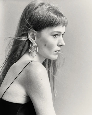 Black and white profile portrait of a woman wearing layered silver hoop earrings and a dark spaghetti-strap top.