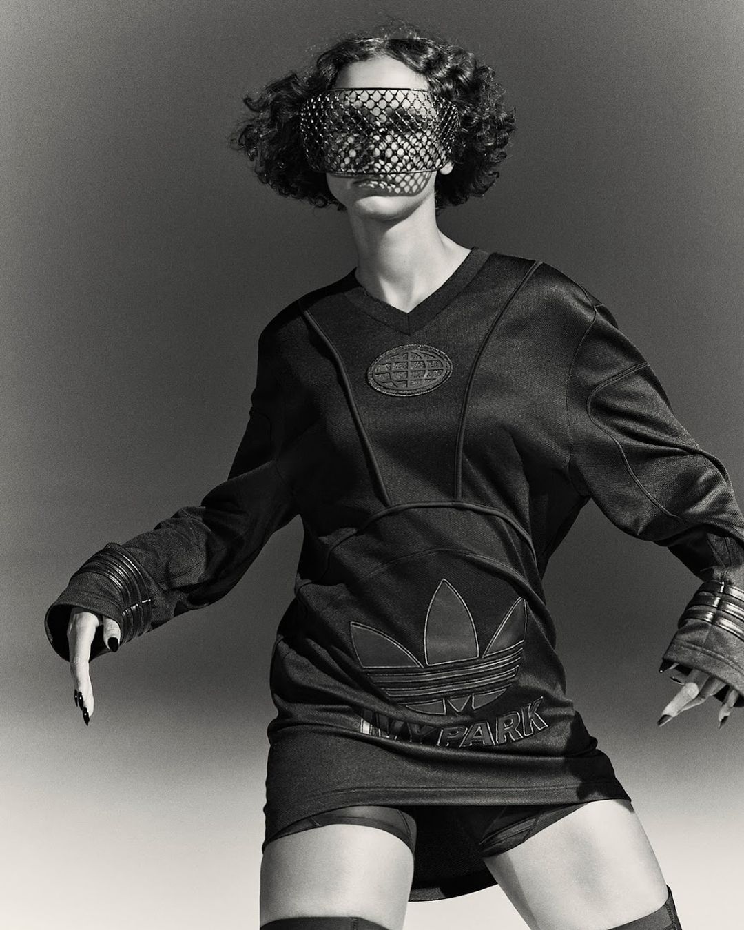 Monochrome portrait of a curly-haired model wearing an Adidas x Ivy Park outfit and face covering, posing against a plain backdrop.