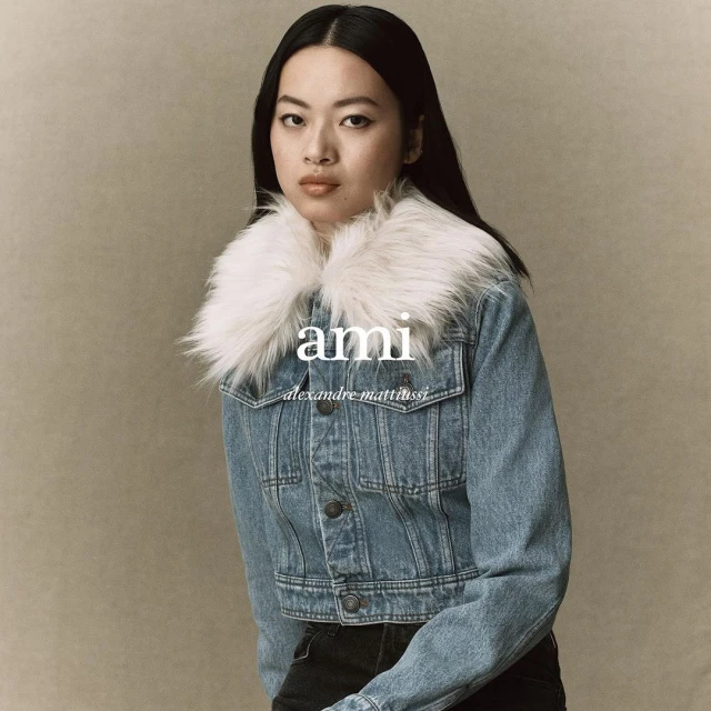Asian woman posing in denim jacket with white fur collar against a neutral background, wearing black pants, with the logo "ami" visible.