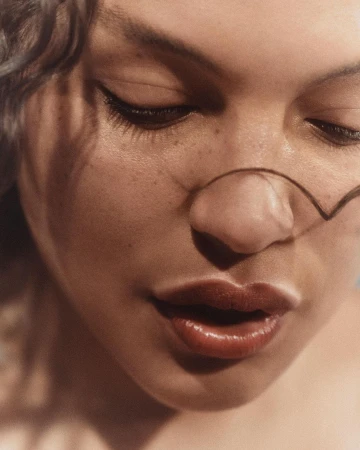 Close-up portrait of a woman with freckles and winged eyeliner, with a single strand of hair crossing her nose, by Melanie + Ramon