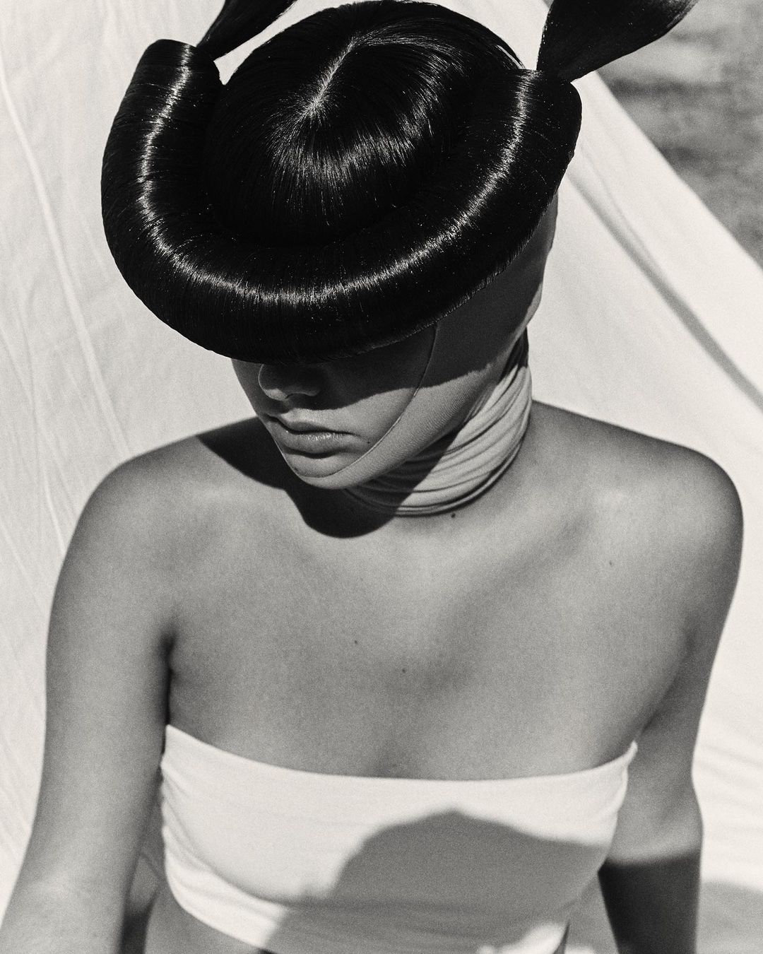 Black and white portrait of an adult woman with a creatively styled updo, wrapped in a bandeau top and neck wrap, against a soft backdrop.