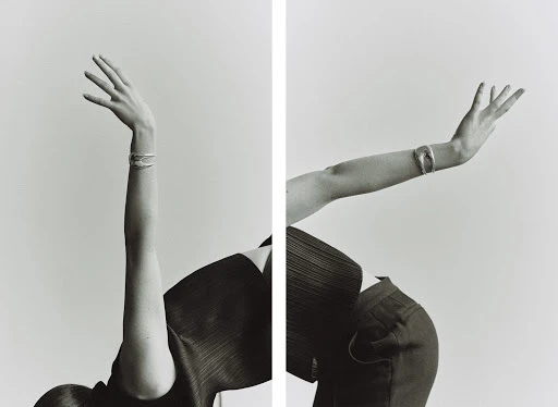 Monochrome shot of a model wearing a bangle with arms raised against a white background creating a mirrored effect.