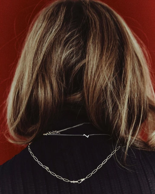 Blonde hair and silver chain necklaces on an adult female against a red background, shot from the back, fashion and beauty.
