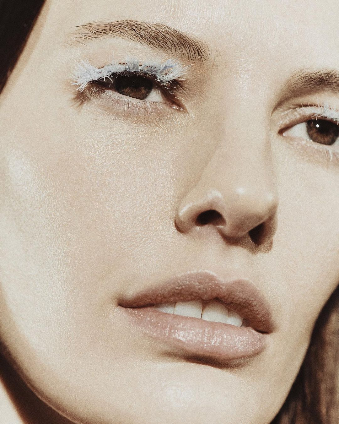 Close-up beauty shot features a fair-skinned woman with creative white eyelashes, full pink lips, and fair skin with an indoor backdrop.