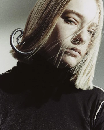 Close-up portrait of a blonde woman wearing a black turtleneck and a large metallic ear cuff by Melanie + Ramon