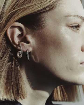 Close-up profile of a woman wearing a spiral diamond ear cuff and a small hoop earring, styled by Melanie + Ramon.