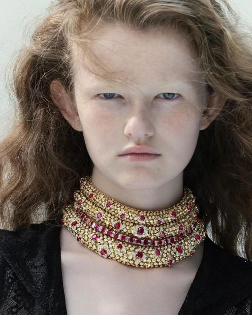 Close-up of a model wearing a gold and ruby choker necklace. The choker is layered and detailed, with a white background.