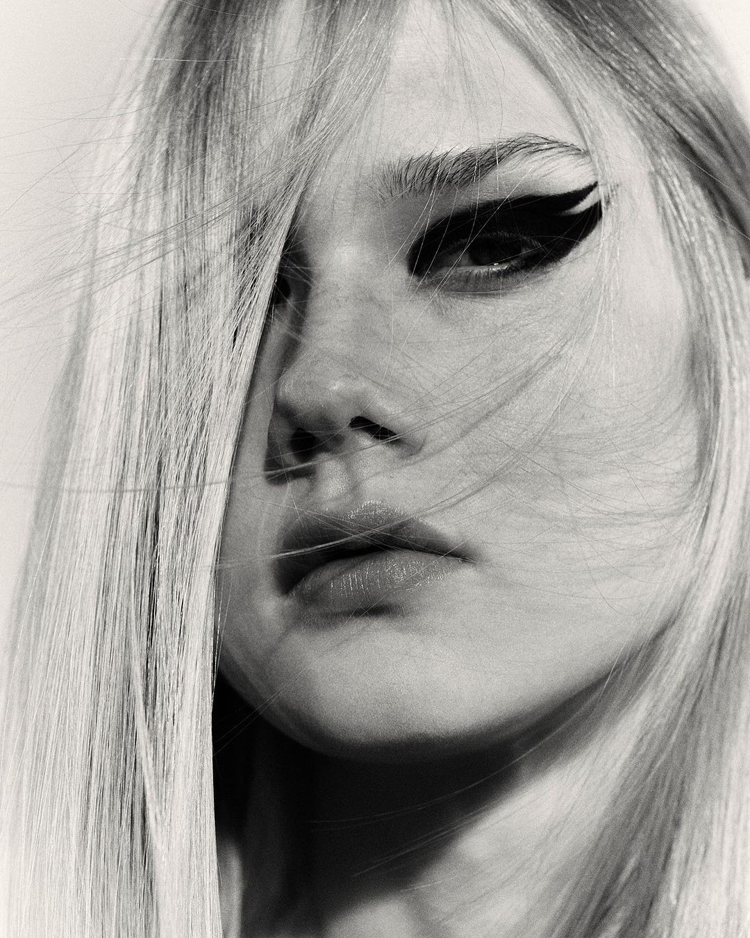 Close-up portrait of a woman with blonde hair across her face and dramatic black winged eyeliner