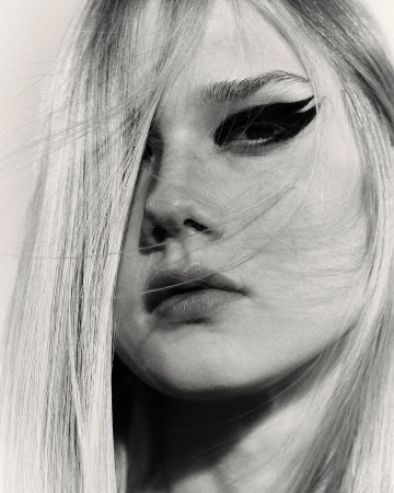 Close-up portrait of a woman with blonde hair across her face and dramatic black winged eyeliner