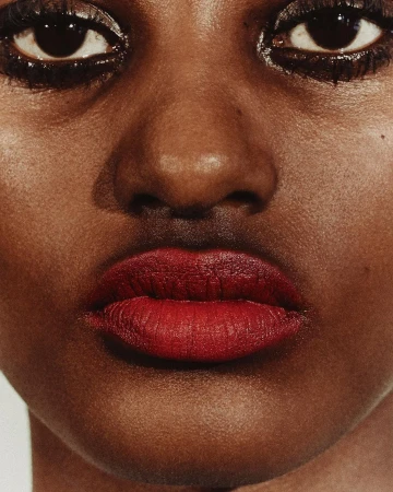 Extreme close-up macro beauty portrait of a Black woman's face highlighting dark red lipstick and heavy eye makeup.
