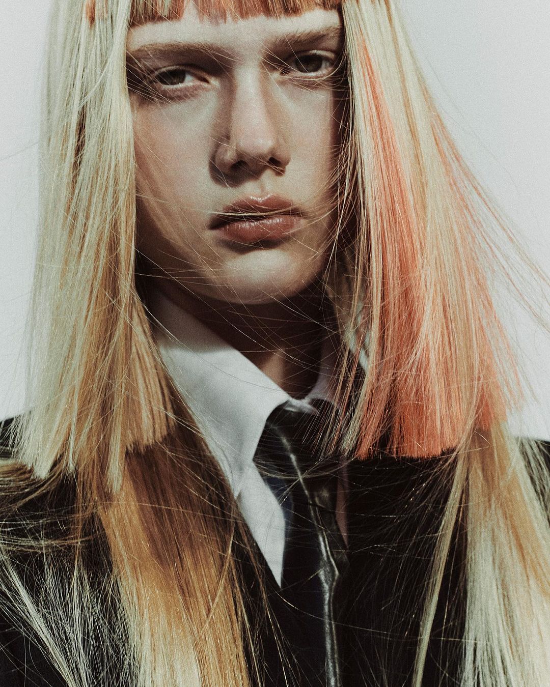 Portrait of a model with blonde hair, white button-down shirt, and black tie against a light background by Melanie + Ramon