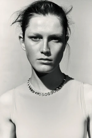 Close-up monochrome portrait of a woman wearing a geometric silver link necklace and sleeveless top against a light background.