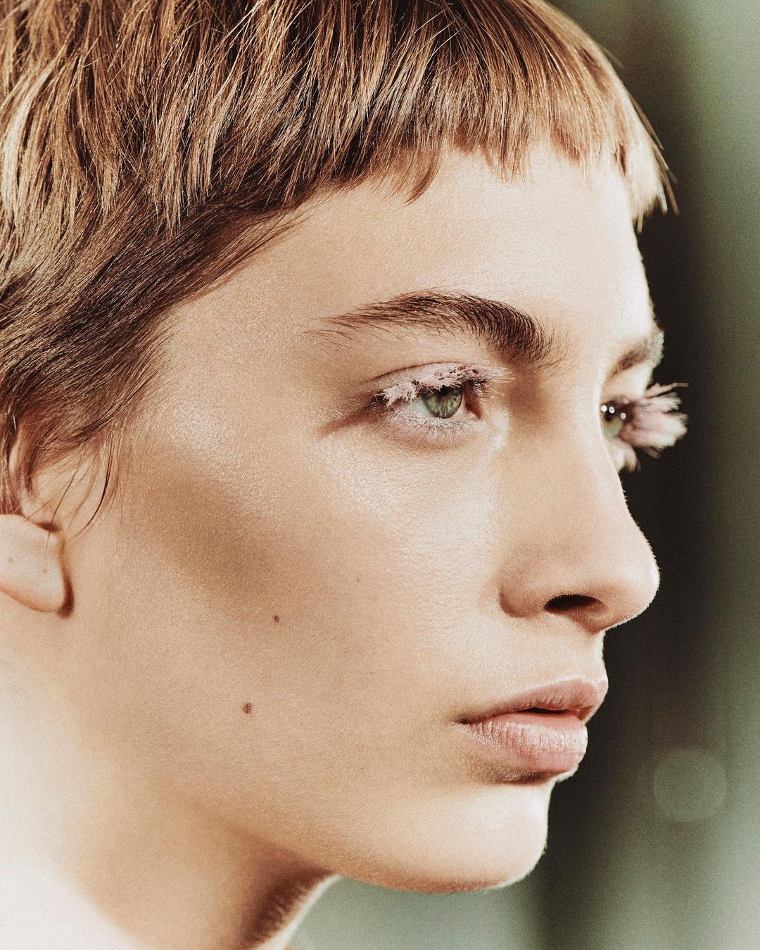 Close-up shot of a person with short, light-brown hair and exaggerated white eyelashes, highlighting their facial features in beauty context.