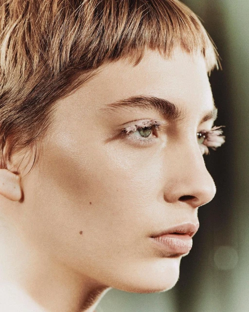 Close-up shot of a person with short, light-brown hair and exaggerated white eyelashes, highlighting their facial features in beauty context.