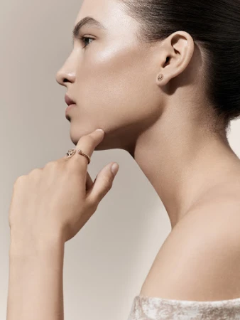 Close-up profile portrait of a woman wearing gold rings and earrings against a plain light background