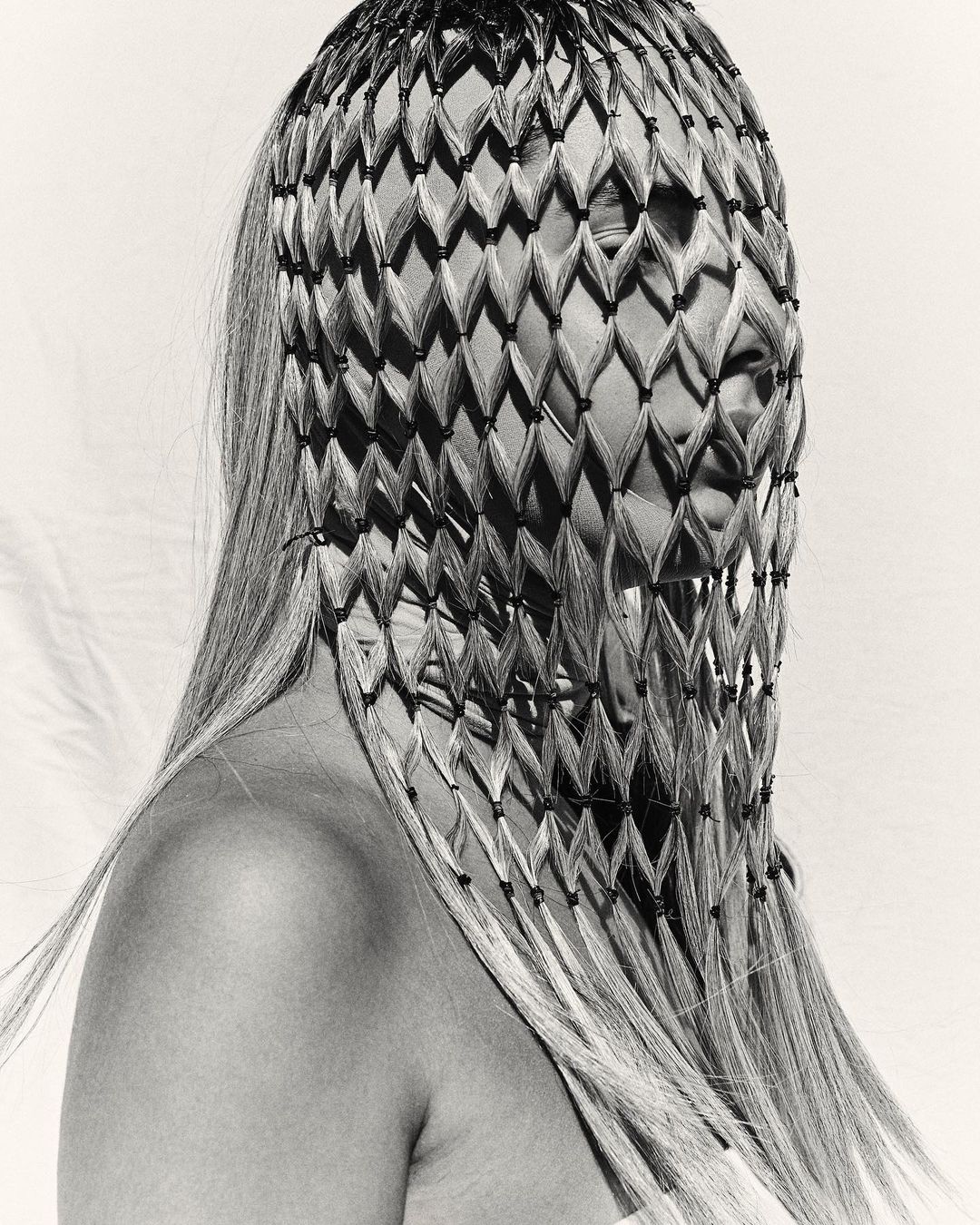 Artistic studio portrait of an adult female with blonde hair wearing a patterned head covering against a white backdrop in black and white.