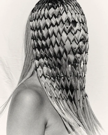 Artistic studio portrait of an adult female with blonde hair wearing a patterned head covering against a white backdrop in black and white.