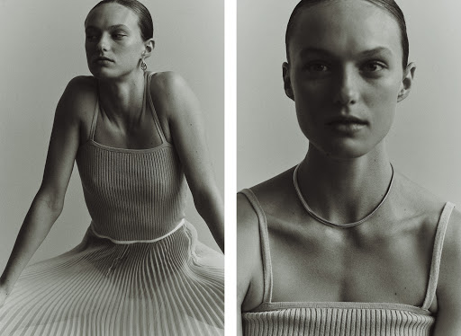Monochrome fashion shot: A woman poses in a ribbed top and pleated skirt against a soft grey backdrop. The look is minimalist and clean.