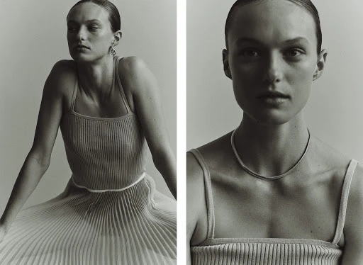 Monochrome fashion shot: A woman poses in a ribbed top and pleated skirt against a soft grey backdrop. The look is minimalist and clean.