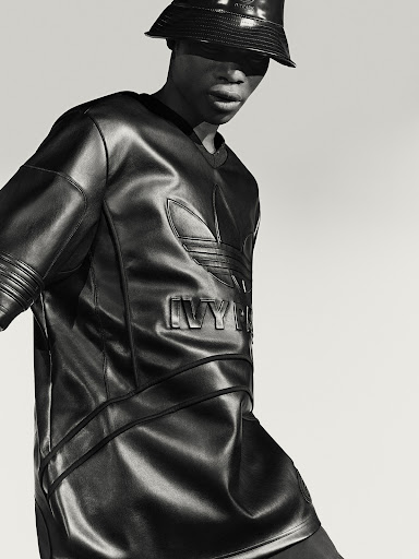 Monochrome studio shot of a Black male model in a black leather Adidas x Ivy Park outfit, including a bucket hat and matching shirt.